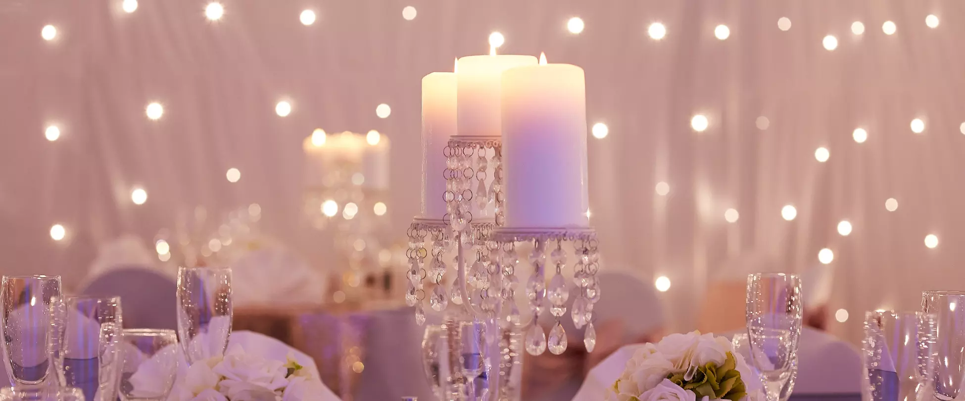 A wedding table centrepiece with 3 large candles on tabletop candelabras. In the background there's a backdrop of lights..